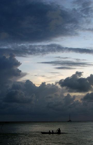 Three figures in canoe on water at dusk with clouds